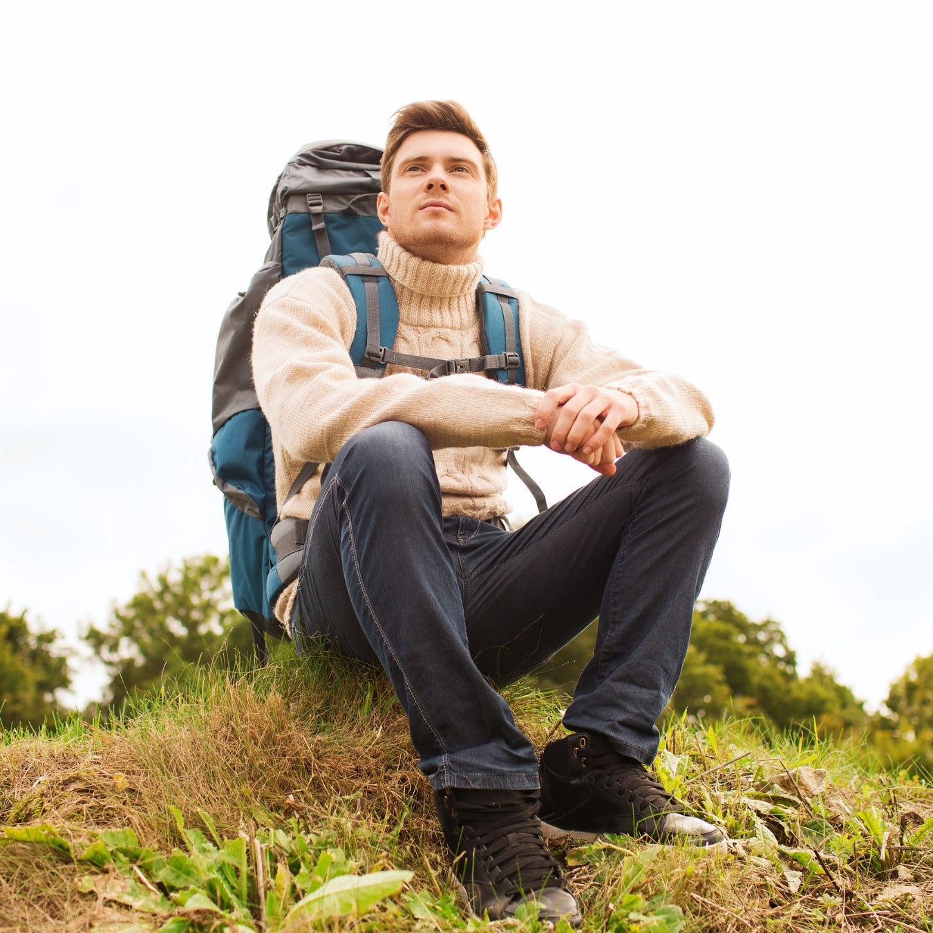 Young male backpacker sitting on grassy hillside looking at scenic horizon view
