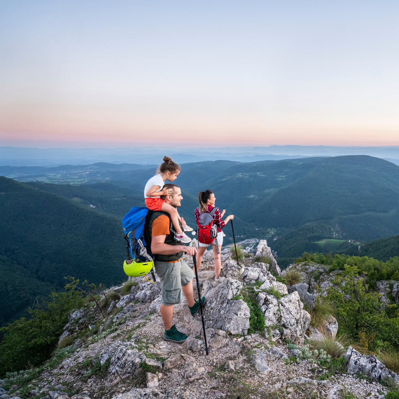 Family with children enjoying sunset view at rocky mountain summit with backpacks
