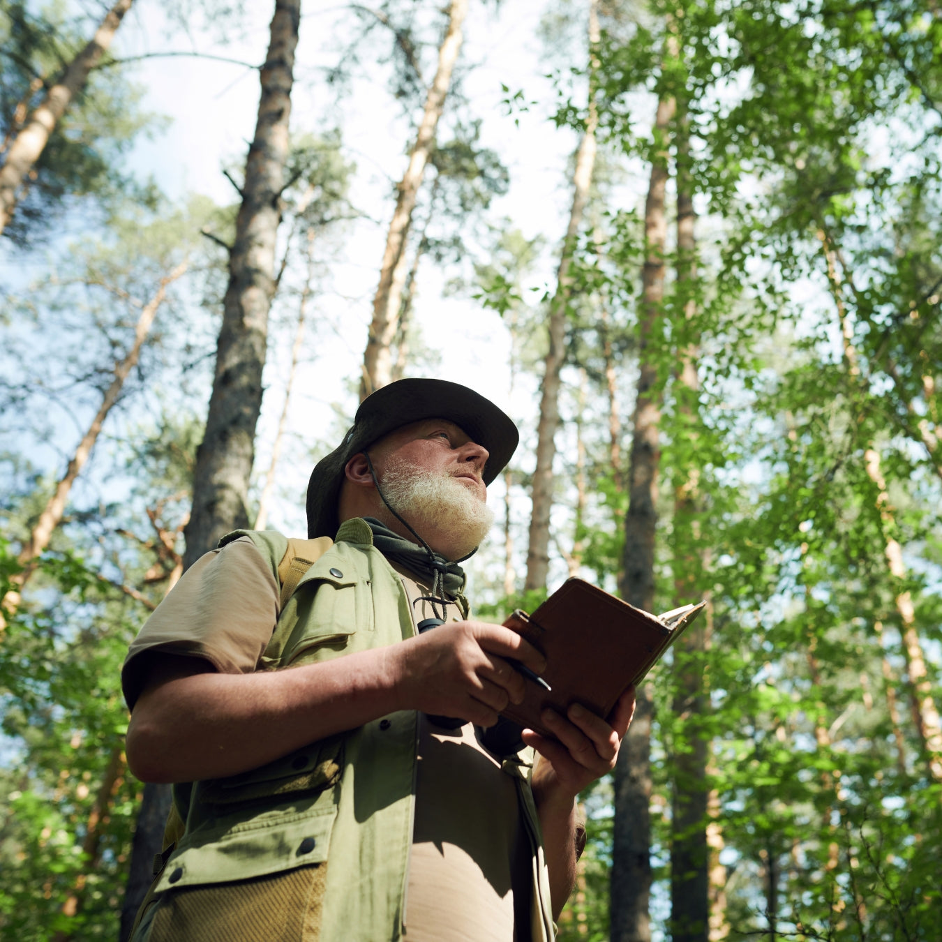 Male hiker in tactical vest and hat writing in journal during outdoor expedition