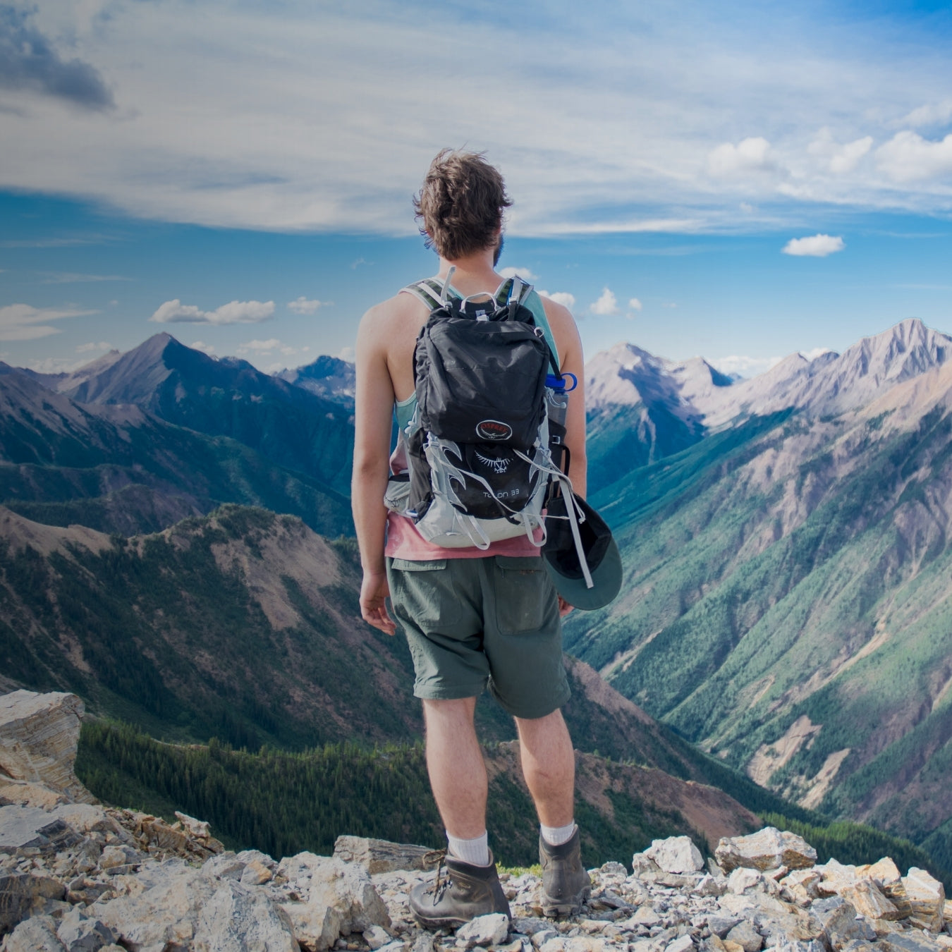Hiker with backpack standing on rocky mountain summit overlooking vast valley
