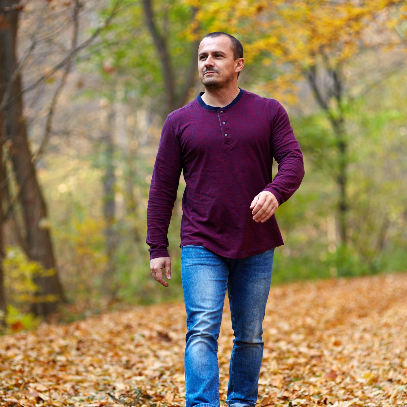 Man walking in a forest during autumn with colorful leaves on the ground.