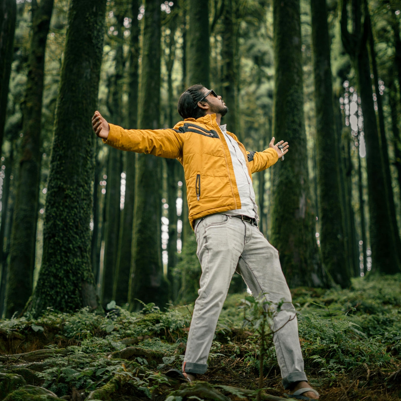 Man in bright yellow jacket with arms outstretched celebrating freedom in forest