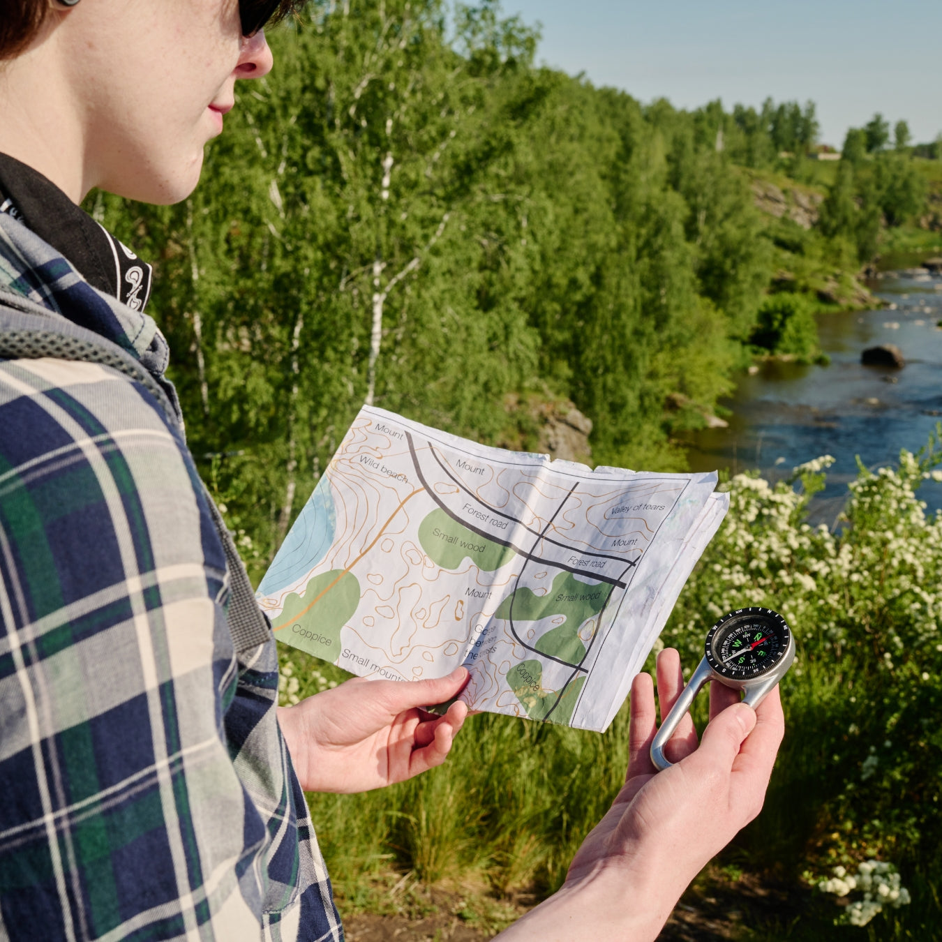 Hiker using topographic map and compass for outdoor trail navigation by river