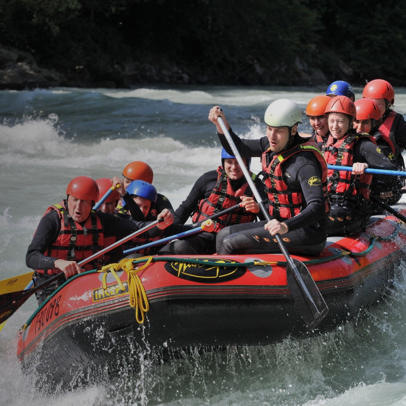 Group of adventurers in safety gear navigating whitewater rapids in inflatable raft
